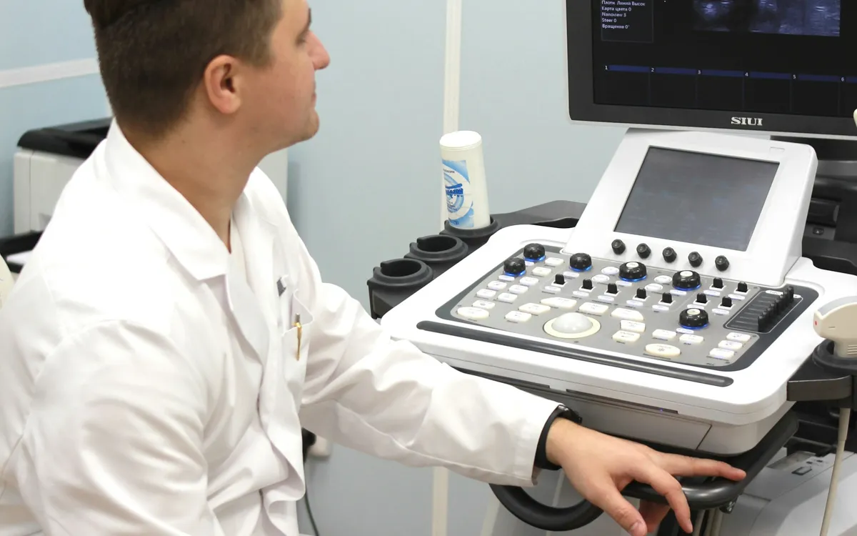 Médico sentado diante de um aparelho de ultrassom em uma sala de exames