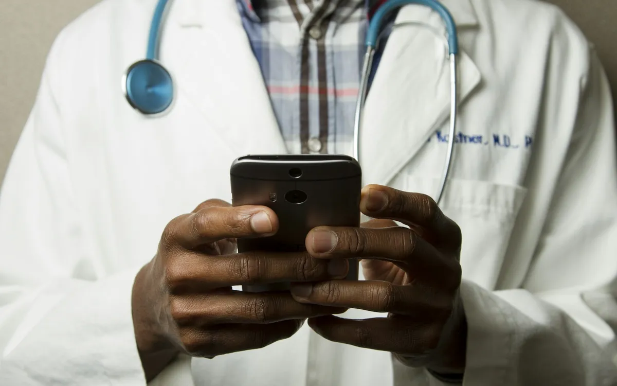 Médico de jaleco segurando um celular