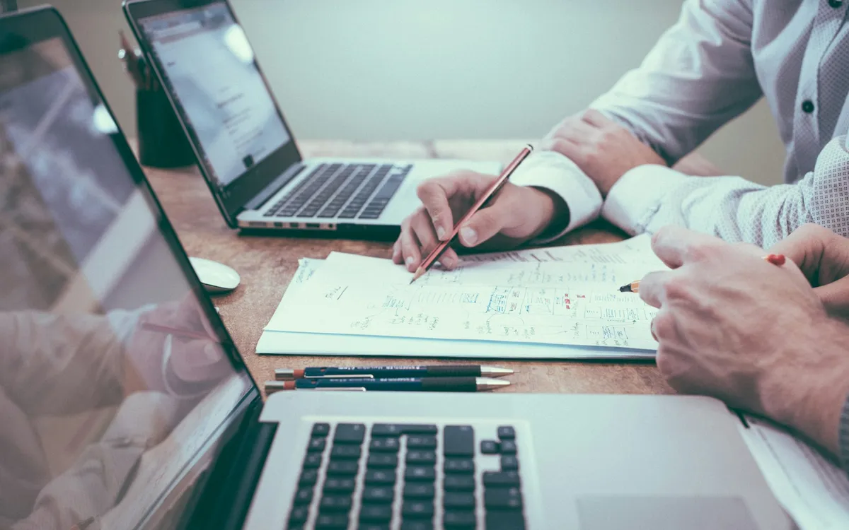 Pessoas trabalhando com notebooks e papéis anotados sobre a mesa
