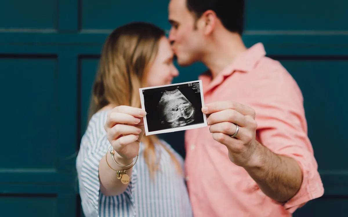 Casal se abraçando e mostrando a foto de um ultrassom do bebê