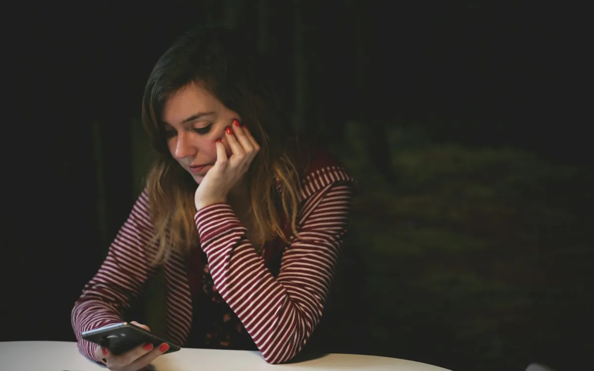 Mulher olhando o celular apoiada em uma mesa