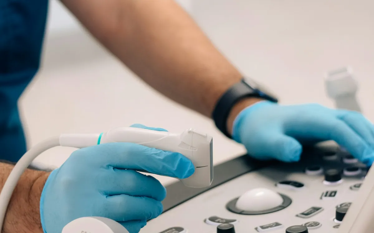 Mão com luva segurando o transdutor de um aparelho de ultrassom
