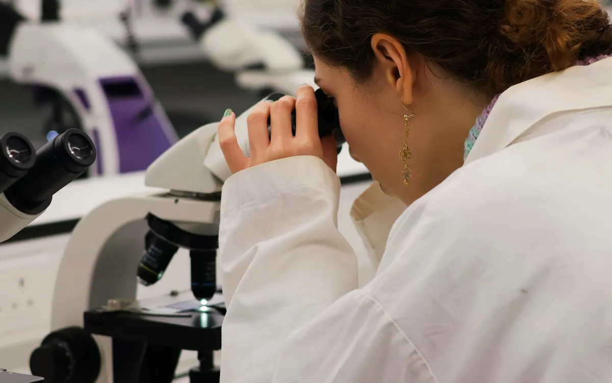 Profissional de laboratório olhando por um microscópio