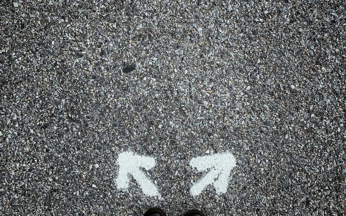Pés sobre o asfalto entre setas apontando para duas direções