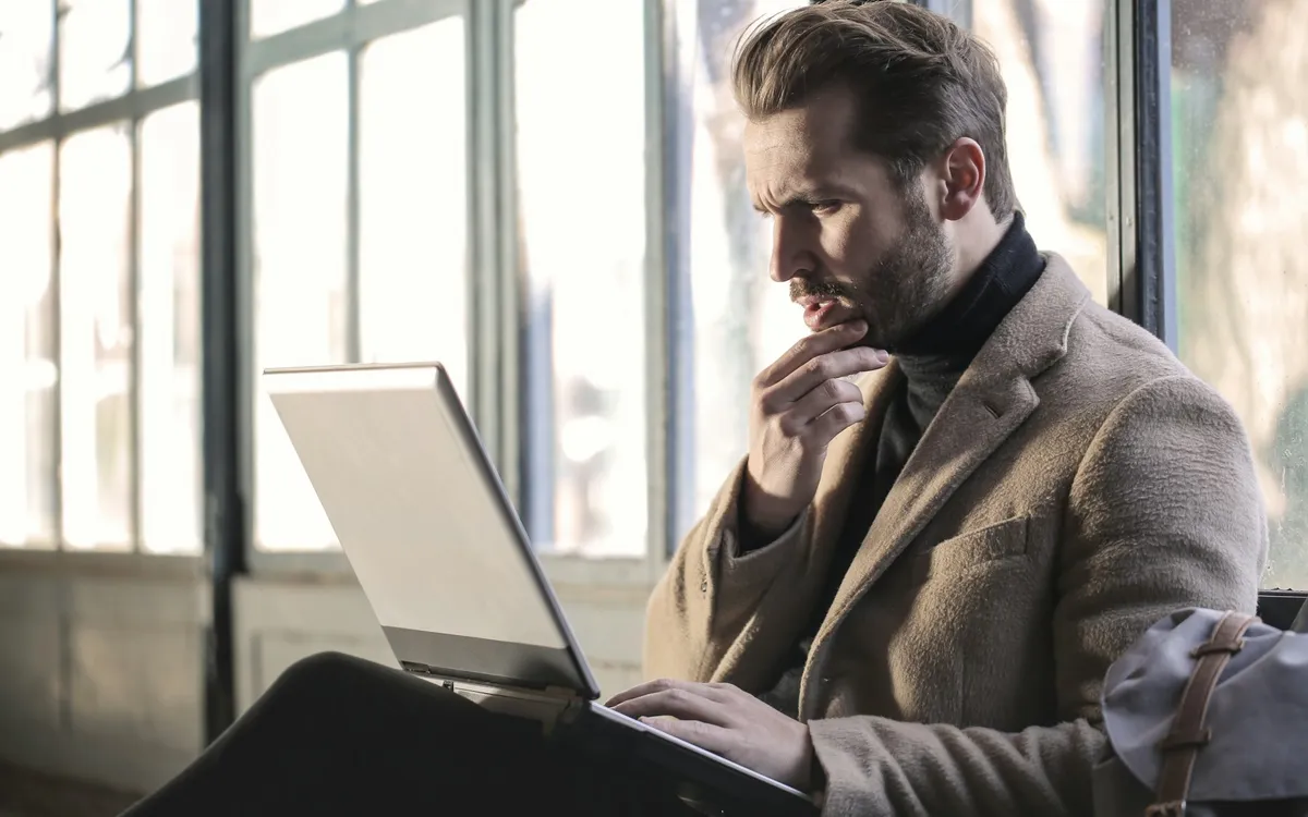 Homem pensativo segurando o queixo diante do computador