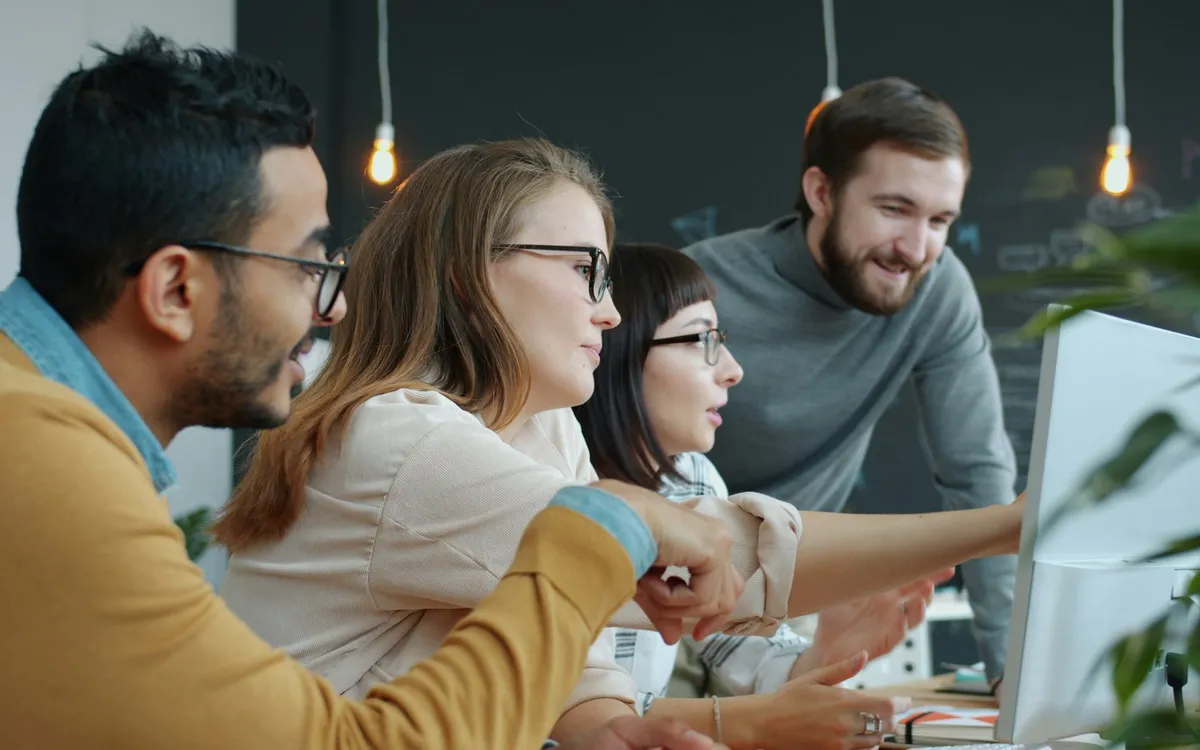 Equipe de uma pequena empresa reunida em volta de um computador