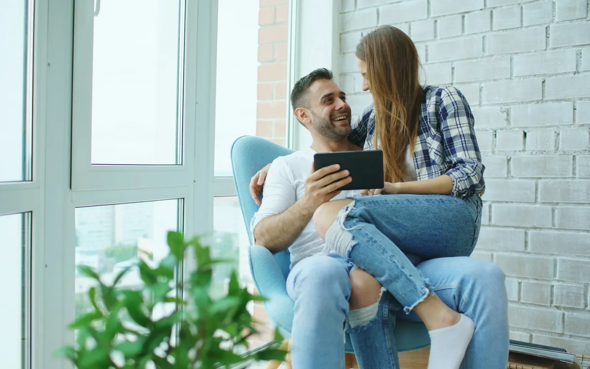 Casal jovem olhando um tablet juntos na poltrona de casa