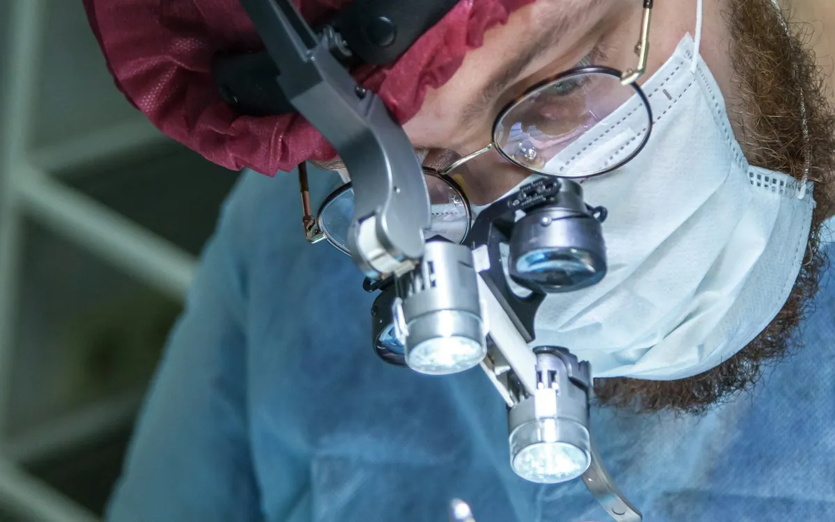 Cirurgião com lupas cirúrgicas e máscara durante um procedimento