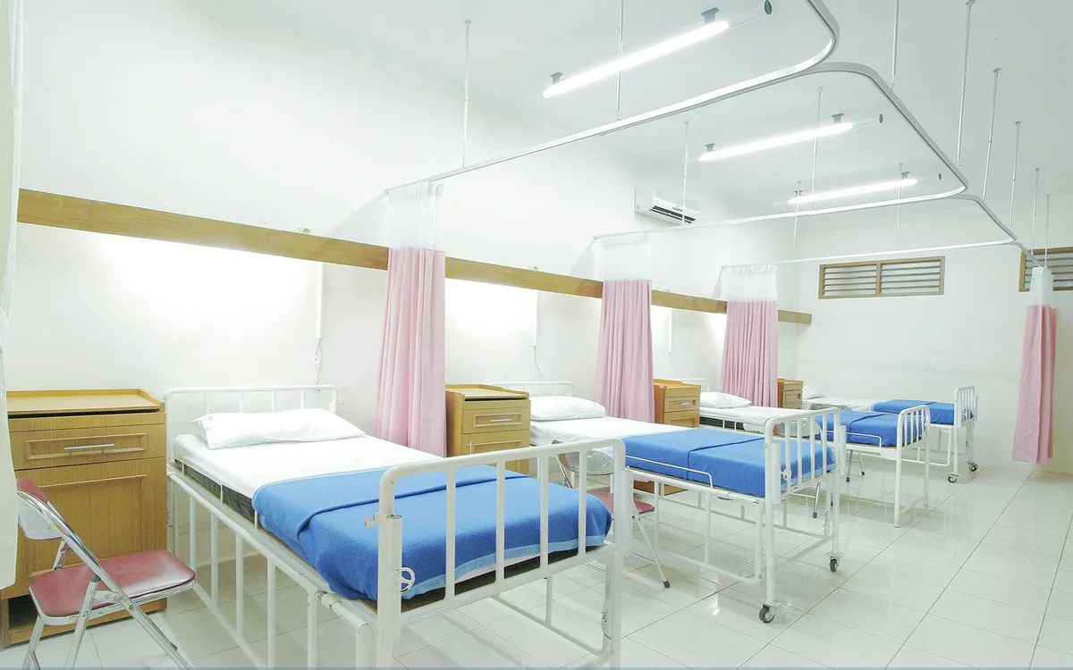 Quarto de hospital com leitos arrumados e cortinas