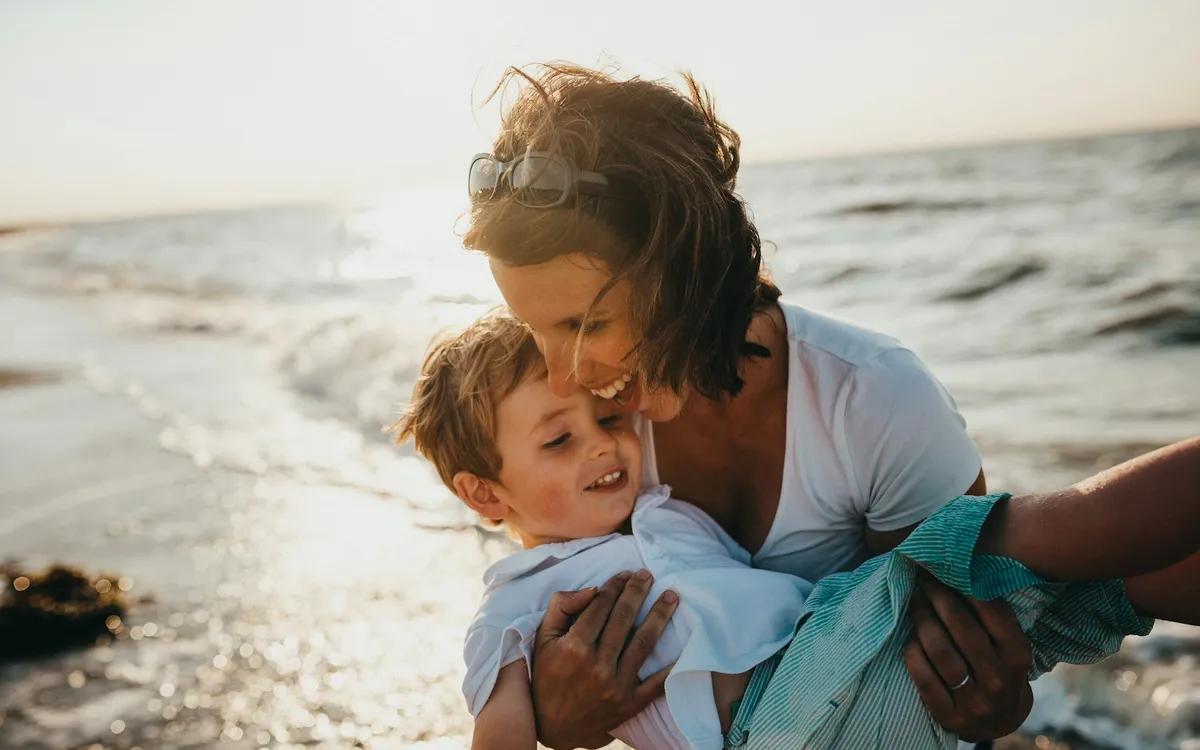 Mãe abraçando o filho pequeno à beira do mar