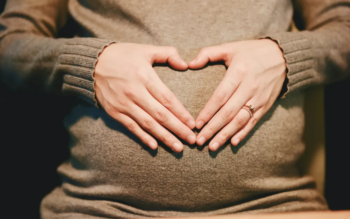 Gestante fazendo um coração com as mãos sobre a barriga