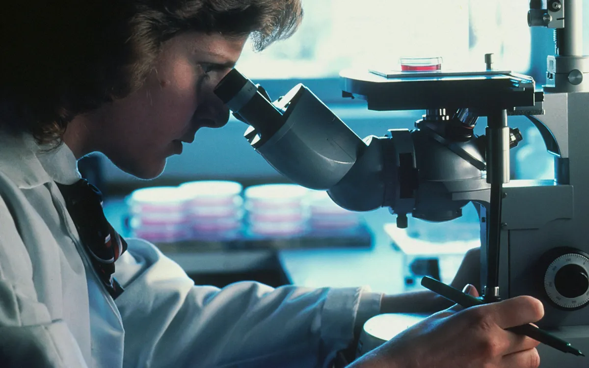 Profissional de jaleco olhando no microscópio de um laboratório